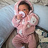 baby, infant, pacifier, hoodie, pink_clothing, polka_dots, blanket, pillow, bed, soft_texture, cozy, cute, child, newborn, sleepwear, indoor, resting, clothing, person, portrait