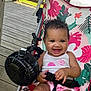 baby, child, smiling, stroller, seatbelt, fan, wooden_deck, outdoor, lake, floral_pattern, pink_clothing, white_tank_top, happy, cute, summer, sunlight, person, infant, seated, playful
