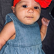 Arielle is registered to the contest to win money with this photo: baby, black_hair, child, closeup, clothing, cute, denim_dress, fabric_background, face, fist, flower, headband, indoors, infant, lying_down, person, portrait, red_flower, skin, young