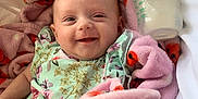 Thea-Rose is registered to the contest to win money with this photo: baby, smiling, blanket, ladybug_pattern, floral_outfit, milk_bottle, infant, cozy, happy, cute, lying_down, pink, white, soft, child, portrait, indoors, bottle, feeding, resting