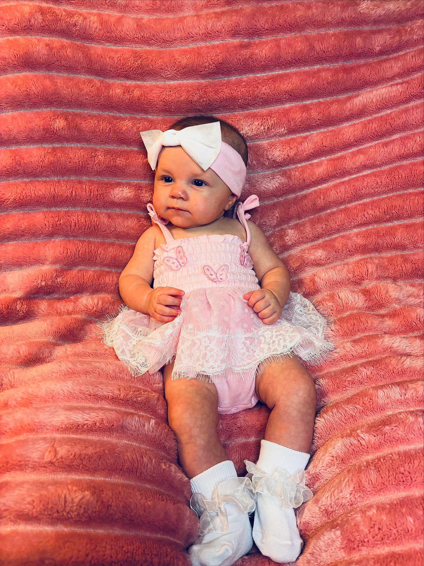 Riley joined the competition — help win amazing prizes! baby, baby_girl, blanket, bow, butterfly, child, clothing, cute, frills, headband, homedecor, infant, lying_down, person, pink_dress, plush, portrait, smiling, socks, soft_texture