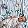 animal_illustrations, baby, child, clothing, colorful, cute, indoors, infant, leaves, lying_down, milestone_blanket, months, onesie, pacifier, peaceful, playful, smiling, toy, wooden_ring, young