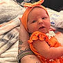 Breylynne joined the competition — help win amazing prizes! baby, infant, orange_clothing, headband, tattoo, arm, blanket, cushion, indoor, person, newborn, cute, portrait, child, soft_texture, hand, colorful, cozy, resting, closeup