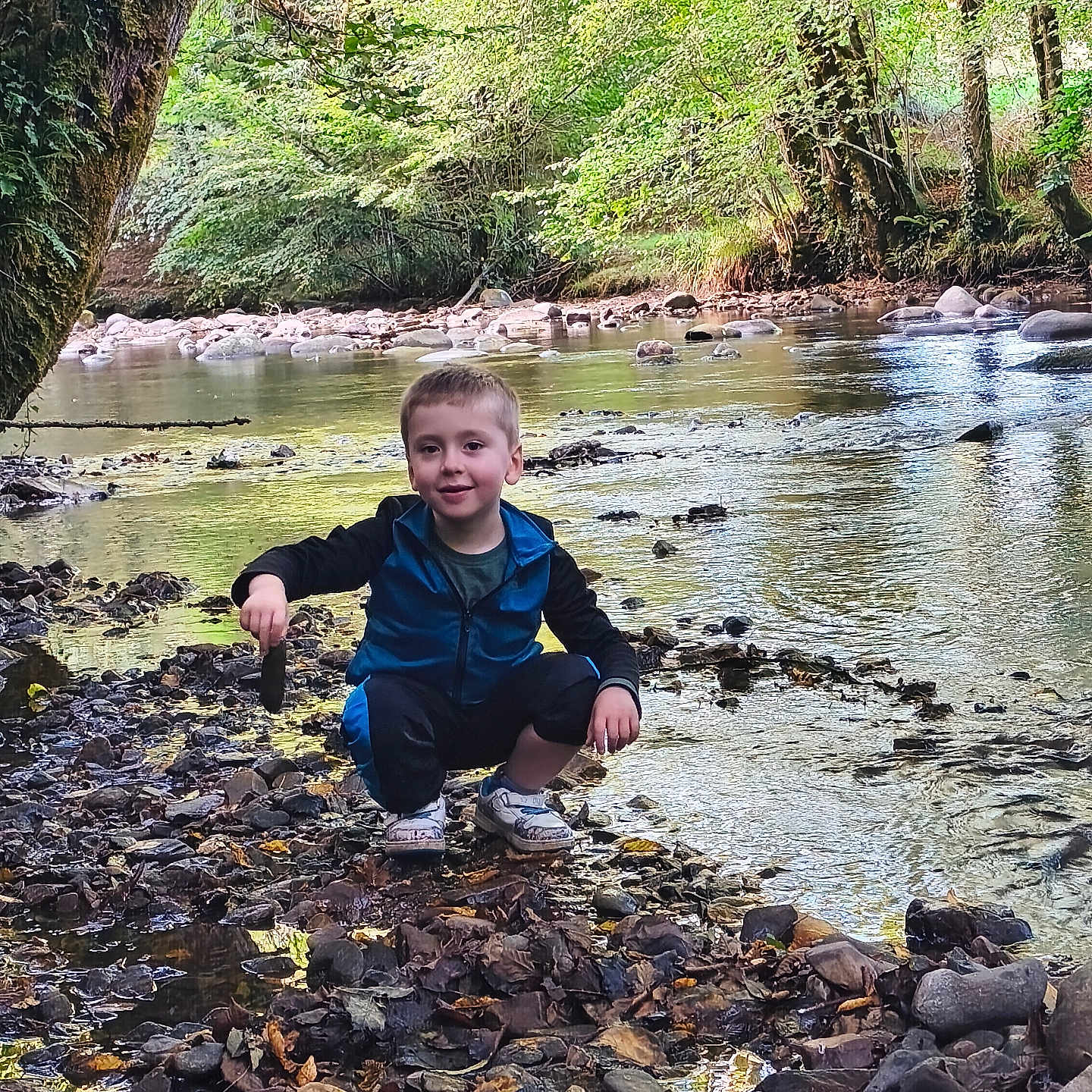 Soan a rejoint le concours — aidez-le/la à gagner de superbes lots ! boy, child, clothing, crouching, daylight, exploration, forest, greenery, leaves, nature, outdoor, play, river, riverbank, rocks, shoes, small_object, smiling, trees, water
