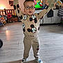 child, boy, glasses, mickey_mouse, sweatshirt, pants, shoes, indoor, living_room, toy, stuffed_animal, flooring, television, furniture, casual_clothing, expression, person, home, playful, standing