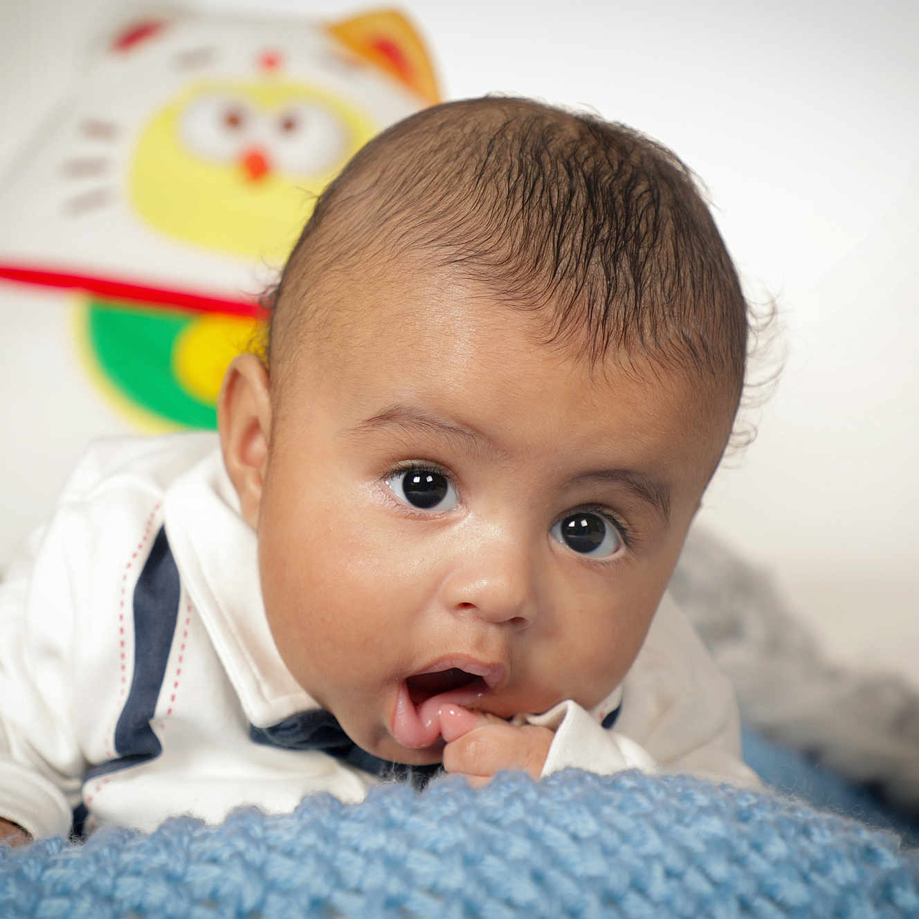 Souleymane a rejoint le concours — aidez-le/la à gagner de superbes lots ! baby, blanket, blue_blanket, child, closeup, clothing, curious, cute, expression, eyes, face, finger_in_mouth, indoors, infant, plush_toy, portrait, skin, soft_texture, white_shirt, young_child