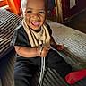 toddler, child, smiling, happy, indoor, couch, clothing, black_shirt, black_pants, red_socks, shoelace, curtain, window, home, portrait, sitting, face, baby, cute, person