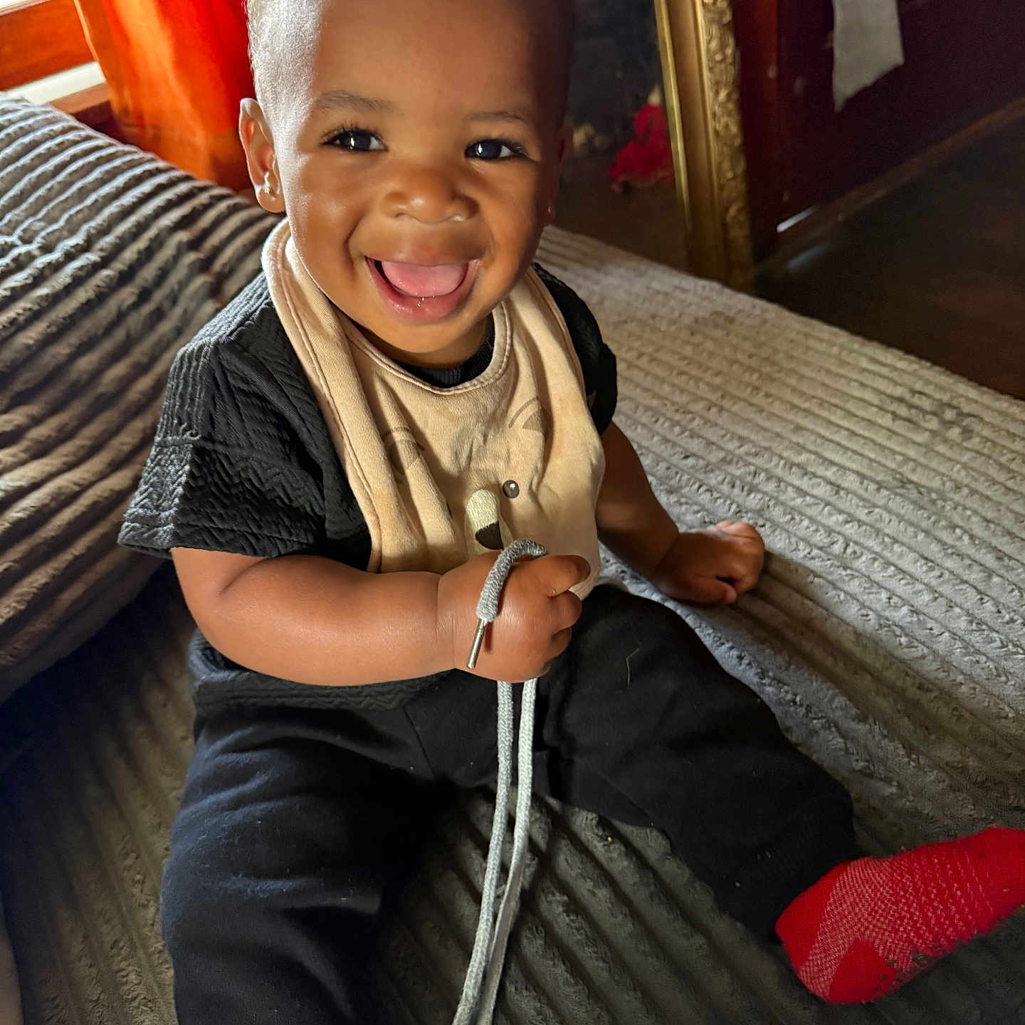 Amirion is registered to the contest to win money with this photo: toddler, child, smiling, happy, indoor, couch, clothing, black_shirt, black_pants, red_socks, shoelace, curtain, window, home, portrait, sitting, face, baby, cute, person