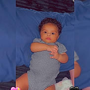 Majesty is registered to the contest to win money with this photo: baby, infant, child, portrait, lying_down, bed, blue_blanket, striped_onesie, clothing, curly_hair, wide_eyes, face, hands, indoor, bedroom, plush_toy, heart_emoji, photography, cozy, cute
