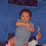 baby, infant, child, portrait, lying_down, bed, blue_blanket, striped_onesie, clothing, curly_hair, wide_eyes, face, hands, indoor, bedroom, plush_toy, heart_emoji, photography, cozy, cute