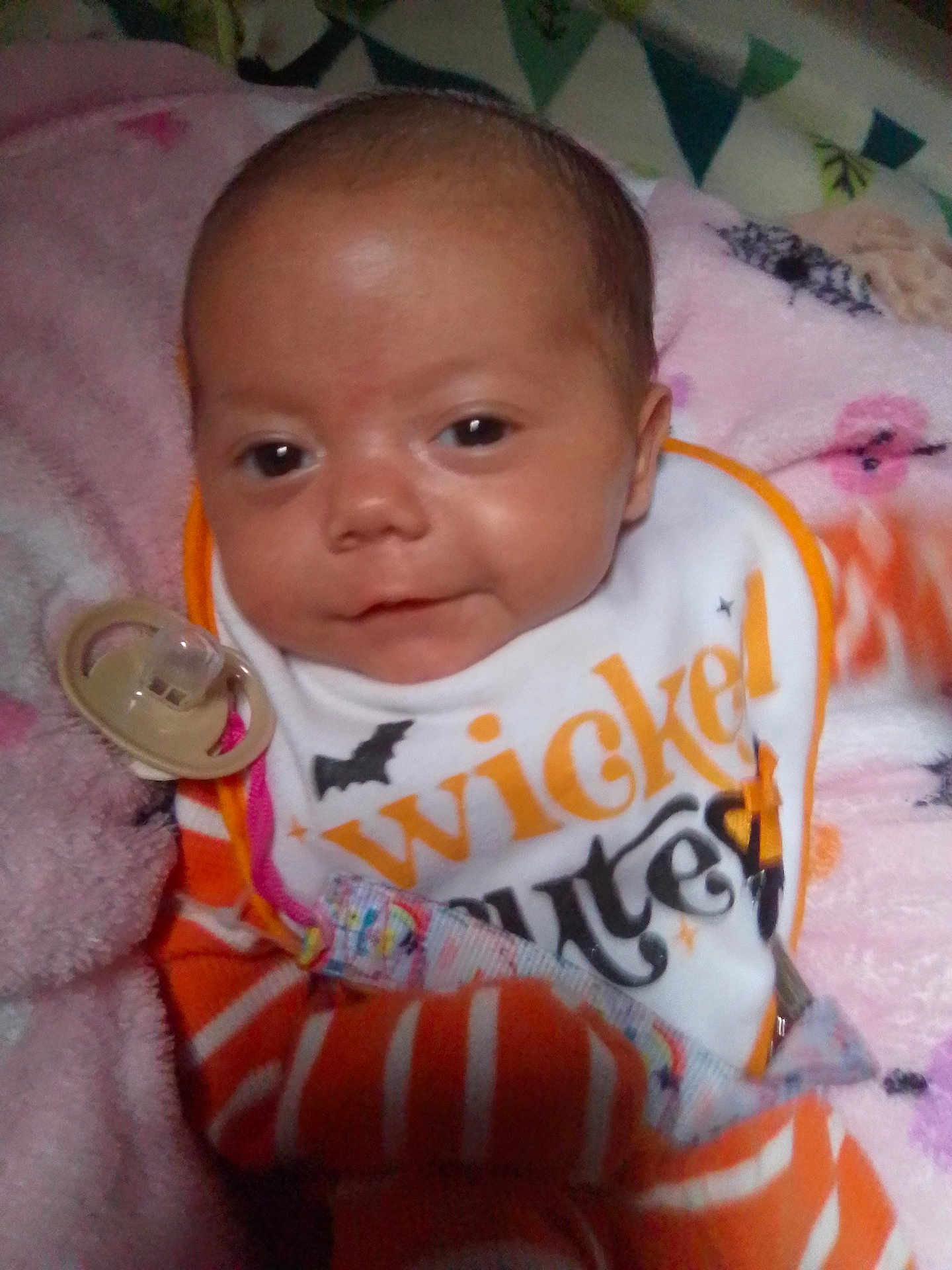 Natalia is registered to the contest to win money with this photo: baby, infant, pacifier, bib, clothing, striped_clothing, blanket, pink_blanket, face, person, cute, lying_down, indoor, newborn, expression, soft_texture, closeup, head, small_baby, sleepwear