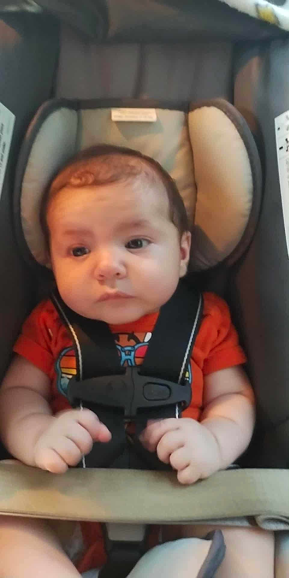 Dustin Lee Willis Jr is registered to the contest to win money with this photo: baby, infant, car_seat, safety_harness, orange_shirt, child, cute, chubby_cheeks, hands, seat, child_safety, portrait, indoor, young_child, person, face, head, expression, car, straps