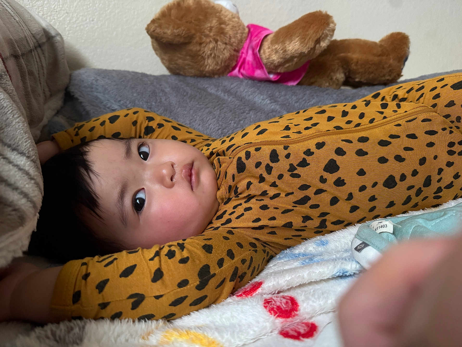 Ria is registered to the contest to win money with this photo: baby, infant, child, bed, blanket, plush_toy, teddy_bear, onesie, leopard_print, sleepwear, cozy, soft_texture, indoors, cute, lying_down, portrait, expression, face, comfort, resting