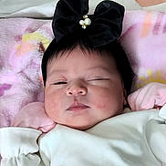 Ari Natasha is registered to the contest to win money with this photo: baby, infant, face, headband, black_bow, white_outfit, blanket, sleepy, portrait, child, cute, soft_texture, pink, pastel_colors, lying_down, indoors, skin, clothing, adorable, young