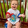 Luca is registered to the contest to win money with this photo: baby, child, smiling, happy, tshirt, dinosaur, outdoor, porch, wood, grass, fence, hair, cute, person, sitting, colorful, greenery, clothing, expression, playful
