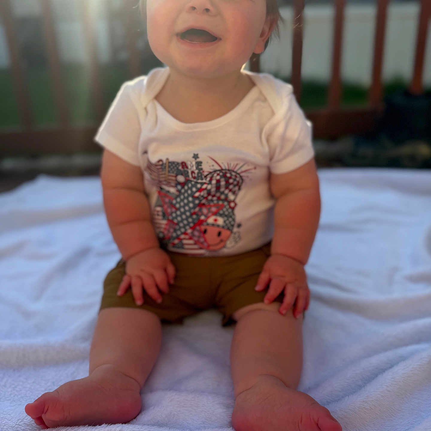 Luca is registered to the contest to win money with this photo: baby, child, smiling, outdoor, blanket, sunlight, fence, happy, sitting, toddler, clothing, shorts, shirt, feet, face, portrait, grass, daylight, skin, cute