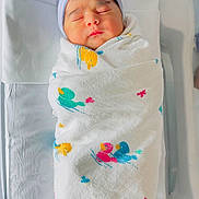 Meera is registered to the contest to win money with this photo: newborn, baby, swaddled, blanket, bow, hat, sleeping, hospital, bassinet, infant, cute, peaceful, child, portrait, soft_light, wrapped, face, headwear, resting, indoors