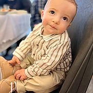 Naim participe au concours pour gagner de l'argent avec cette photo : baby, beige_pants, casual_clothing, chair, child, close_up, curious_eyes, cute, expression, face, human, indoor, person, portrait, sitting, soft_lighting, striped_shirt, tan_shoes, toddler, young_child