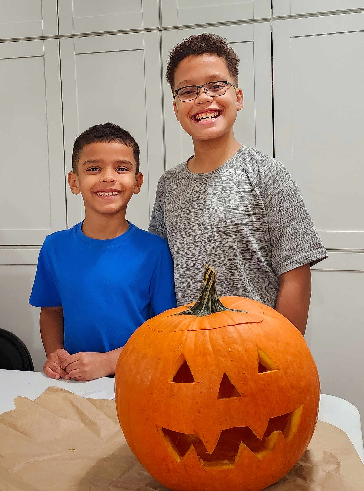 Kyan And Bo joined the competition — help win amazing prizes! child, children, smiling, jack_o_lantern, pumpkin, carved_pumpkin, halloween, kitchen, table, happy, orange, face, boy, glasses, short_hair, gray_shirt, blue_shirt, indoor, celebration, holiday