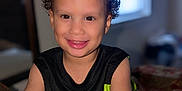Isaiah is registered to the contest to win money with this photo: child, toddler, smiling, curly_hair, indoor, sitting, black_shirt, neon_green, bright_colors, happy, portrait, face, dimples, window, light, cozy, person, clothing, skin, young