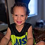 child, toddler, smiling, curly_hair, indoor, sitting, black_shirt, neon_green, bright_colors, happy, portrait, face, dimples, window, light, cozy, person, clothing, skin, young