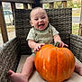 baby, infant, pumpkin, overalls, wicker_chair, porch, outdoor, smile, happy, laughing, hands, feet, cushion, seasonal, autumn, orange, vegetable, sitting, portrait, cute