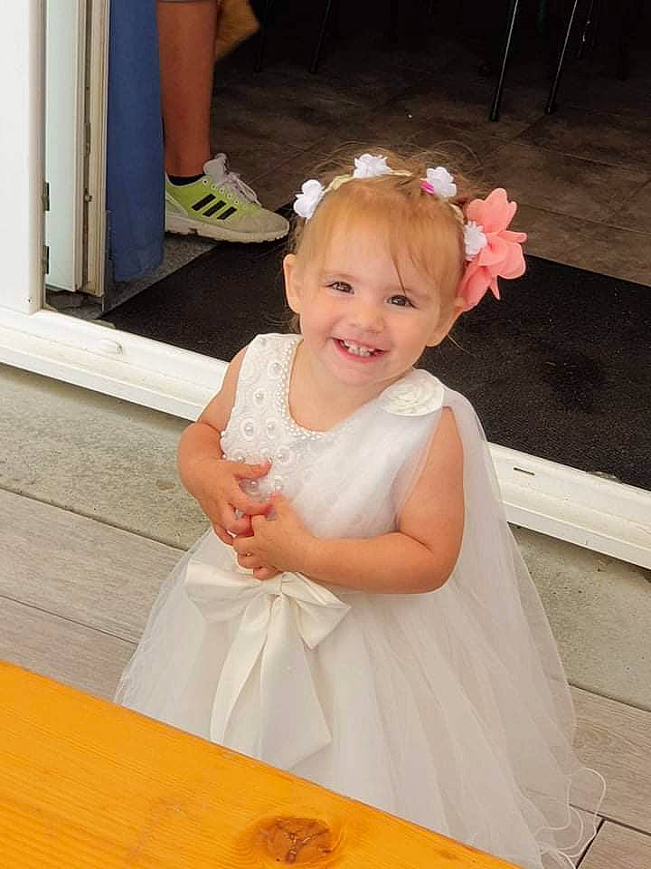 Maëline participe au concours pour gagner de l'argent avec cette photo : baby_toddler_clothing, blond, bridal_accessory, child, day_dress, dress, embellishment, event, flower, formal_wear, fun, happy, headband, headpiece, joy, person, pink, skin, smile, table