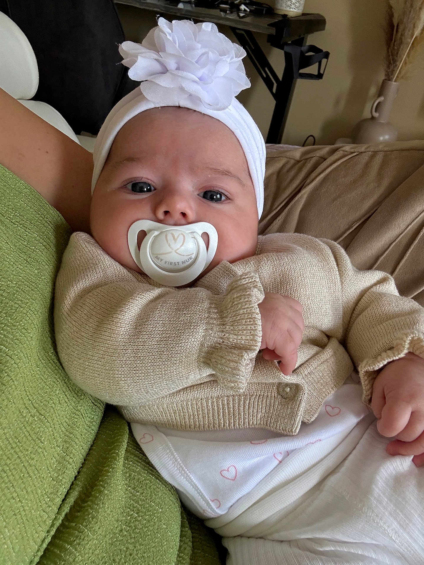 Alma a rejoint le concours — aidez-le/la à gagner de superbes lots ! baby, infant, pacifier, headband, flower, sweater, knitwear, white_clothing, heart_pattern, blanket, green_blanket, indoor, couch, resting, cute, child, person, closeup, portrait, soft_lighting