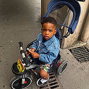 Esaïe participe au concours pour gagner de l'argent avec cette photo : child, clothing, concrete, denim_jacket, expression, grate, handlebar, lollipop, outdoor, person, shoes, shorts, sidewalk, street, toddler, toy, tricycle, urban, vehicle, wheel