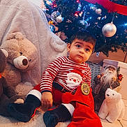 Jayro participe au concours pour gagner de l'argent avec cette photo : blanket, child, christmas_tree, cute, decorations, festive, floor, gift_bag, holiday, indoor, lights, plush_toy, polar_bear_toy, red_clothing, santa_figurine, striped_shirt, teddy_bear, toddler, toy, winter