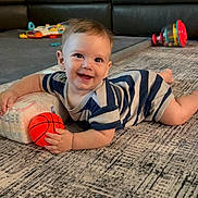 Kai is registered to the contest to win money with this photo: baby, child, smiling, striped_onesie, toy_basketball, carpet, living_room, sofa, colorful_toys, floor_play, happy, infant, crawling, cute, indoor, home, playtime, young_child, person, toddler