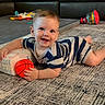 baby, child, smiling, striped_onesie, toy_basketball, carpet, living_room, sofa, colorful_toys, floor_play, happy, infant, crawling, cute, indoor, home, playtime, young_child, person, toddler