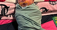 Jahmyr joined the competition — help win amazing prizes! newborn, baby, infant, swaddled, pacifier, portrait, face, eyes, sleepy, lying_down, blanket, bed, textile, green_clothing, pink, black, colorful, indoors, close_up, photography