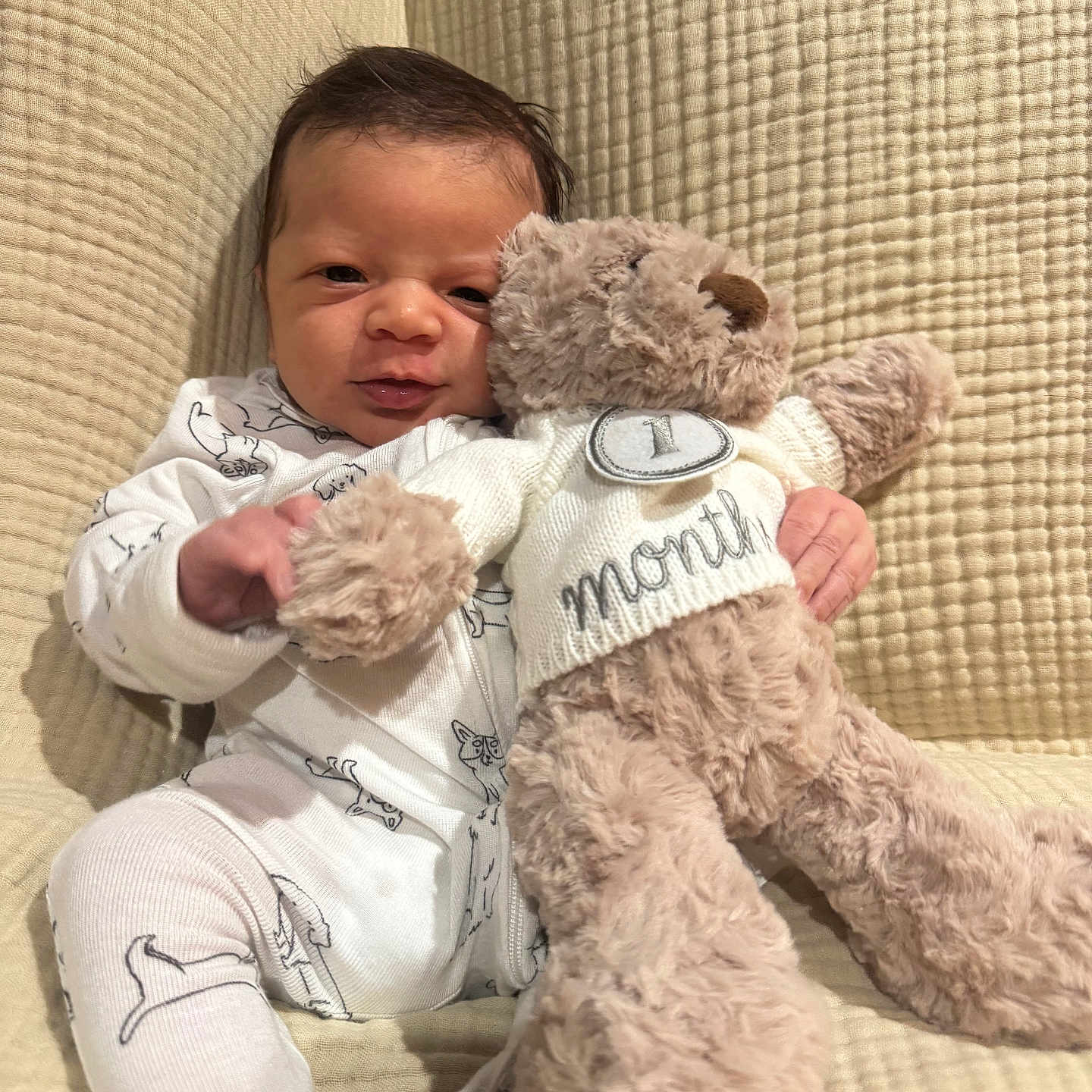 Jahmyr is registered to the contest to win money with this photo: newborn, baby, child, teddy_bear, plush_toy, cuddling, sitting, portrait, smiling, indoors, blanket, cushion, onesie, clothing, nursery, cozy, soft_toy, face, text_on_clothing, warm_lighting