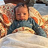 Jahmyr is registered to the contest to win money with this photo: baby, infant, child, portrait, face, eyes, smiling, sitting, blanket, bedding, floral_pattern, blue_clothing, onesie, indoors, bedroom, home, soft_lighting, closeup, baby_clothing, cozy