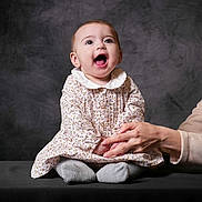 Mencia participe au concours pour gagner de l'argent avec cette photo : adult, baby, background, child, clothing, cute, dress, expression, hand, happy, holding, joy, person, portrait, seated, smile, socks, studio, table, toddler