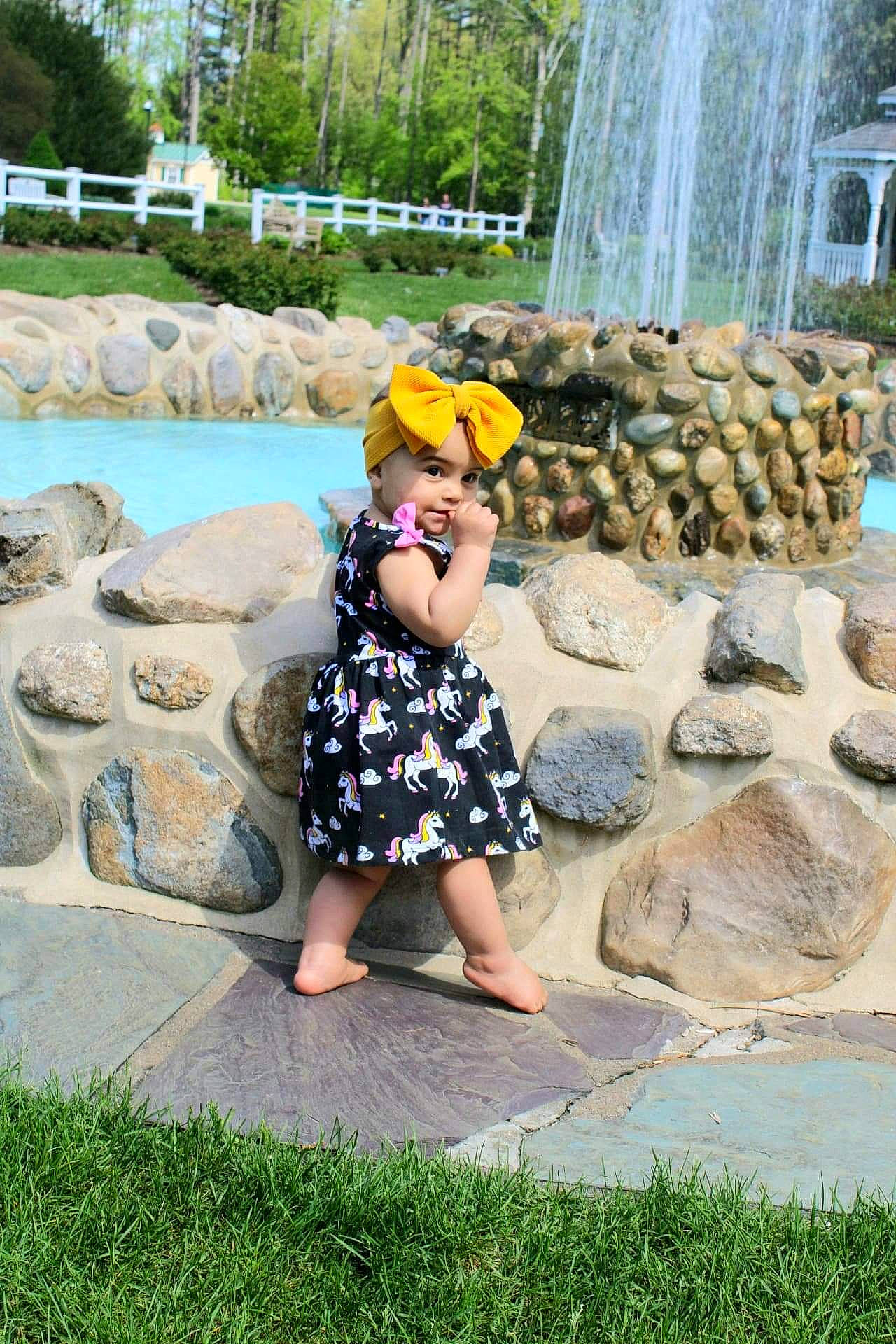 Jazlyn is registered to the contest to win money with this photo: botany, child, fountain, fun, grass, green, hat, headwear, leisure, nature, person, plant, public_space, recreation, summer, toddler, travel, tree, wall, water