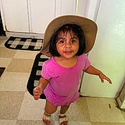 Victoria is registered to the contest to win money with this photo: child, toddler, girl, cowboy_hat, pink_shirt, smiling, portrait, indoor, kitchen, floor, tile_floor, cabinet, door, rug, sandals, standing, short_hair, dark_hair, looking_at_camera, playful