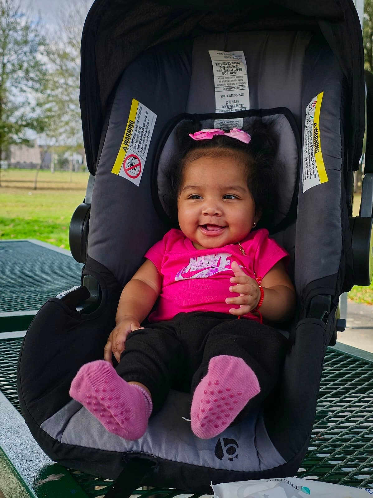 Isabel Cristina joined the competition — help win amazing prizes! baby, smiling, pink_bow, pink_socks, car_seat, outdoor, picnic_table, child, happy, toddler, clothing, seat, person, park, nature, accessory, cute, infant, daylight, playful