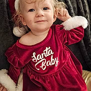 Phoebe joined the competition — help win amazing prizes! toddler, child, smiling, curly_hair, red_dress, santa_hat, holiday_clothing, indoor, portrait, cute, festive, soft_texture, blanket, white_fur, happy, baby, person, face, sitting, playful
