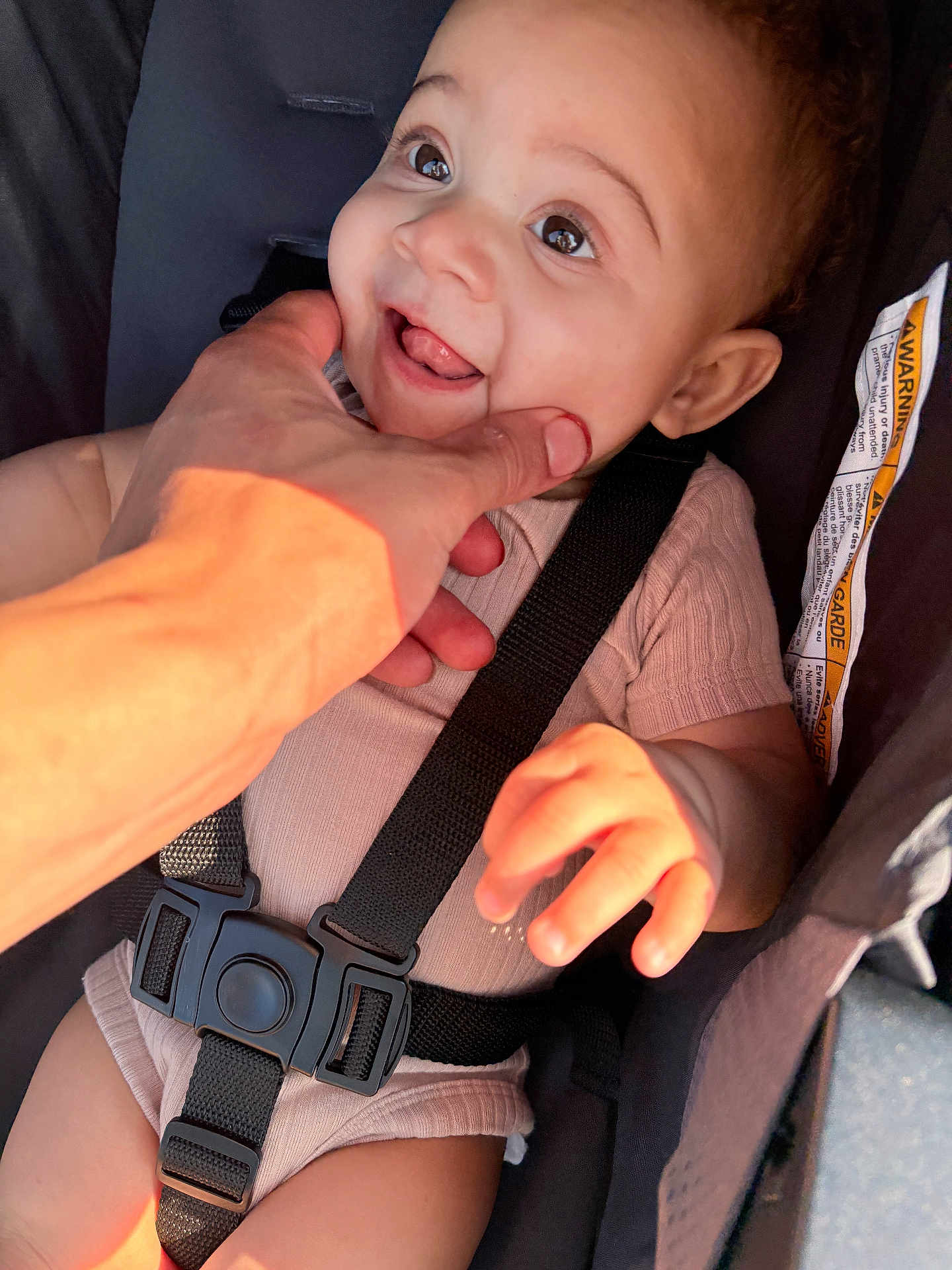 Evealynn is registered to the contest to win money with this photo: baby, child, car_seat, seat_belt, hand, smile, tongue, cute, infant, skin, clothing, straps, safety, playful, expression, person, closeup, sunlight, happy, cheek