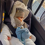 Zayan participe au concours pour gagner de l'argent avec cette photo : baby, child, car_seat, winter_clothing, hat, pacifier, plush_toy, scarf, white_suit, car_interior, seatbelt, window, child_protection, cute, infant, warm, outdoor_clothing, sitting, portrait, cozy