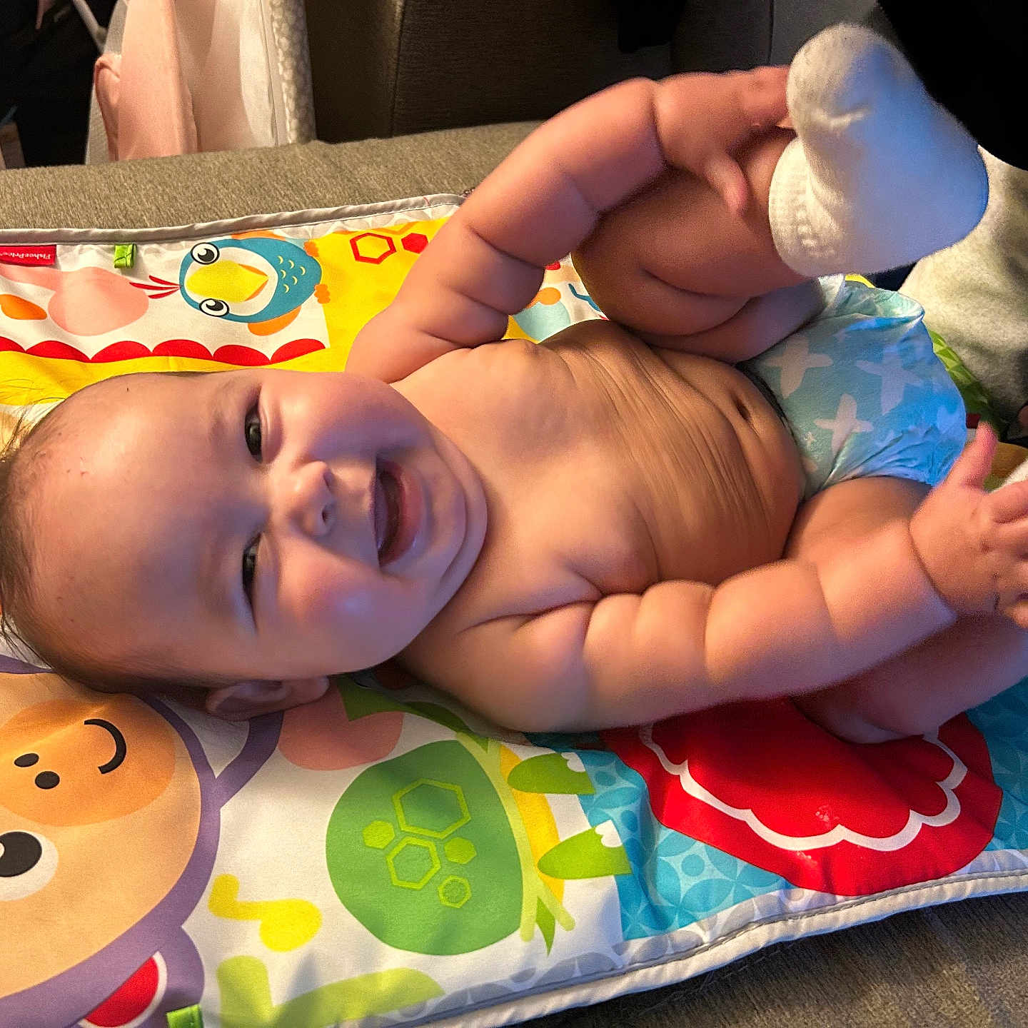 Celestia is registered to the contest to win money with this photo: baby, smiling, chubby, play_mat, colorful, diaper, sock, indoor, happy, cute, child, infant, lying_down, hands, feet, face, skin, fun, joy, person
