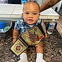 baby, casual, child, curious, door, floor, high_chair, home, indoor, kitchen, marble_countertop, person, plaid_shirt, plastic_container, smiling, table, tattooed_arm, water_bottle, white_socks, wwe_championship_belt