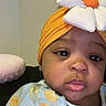 baby, child, face, headwrap, flower, orange, blue_clothing, floral_pattern, indoor, portrait, cute, infant, closeup, looking, young_child, head_accessory, expression, skin, person, apparel