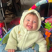 Avery joined the competition — help win amazing prizes! baby, child, onesie, green_clothing, infant, tongue_out, smiling, indoor, baby_toys, activity_center, colorful, playful, cute, happy, face, hand, seat, hood, person, young_child