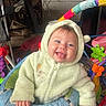 baby, child, onesie, green_clothing, infant, tongue_out, smiling, indoor, baby_toys, activity_center, colorful, playful, cute, happy, face, hand, seat, hood, person, young_child