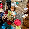 child, toddler, basket, plastic_lids, floor, kitchen, container, messy, curious, standing, sitting, clothing, toy, household, indoor, playful, reaching, flooring, broom, storage