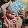 toddler, child, diaper, hand, pink_shirt, indoor, kitchen, person, curious, expression, clutter, furniture, adult_hand, playful, hat, baby, room, light, holding, casual