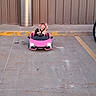 Avery joined the competition — help win amazing prizes! toddler, child, toy_car, pink, parking_lot, concrete, metal_cylinder, building_wall, excited, happy, outdoor, daylight, vehicle, small_car, hands_up, sidewalk, curb, yellow_paint, casual_clothing, fun
